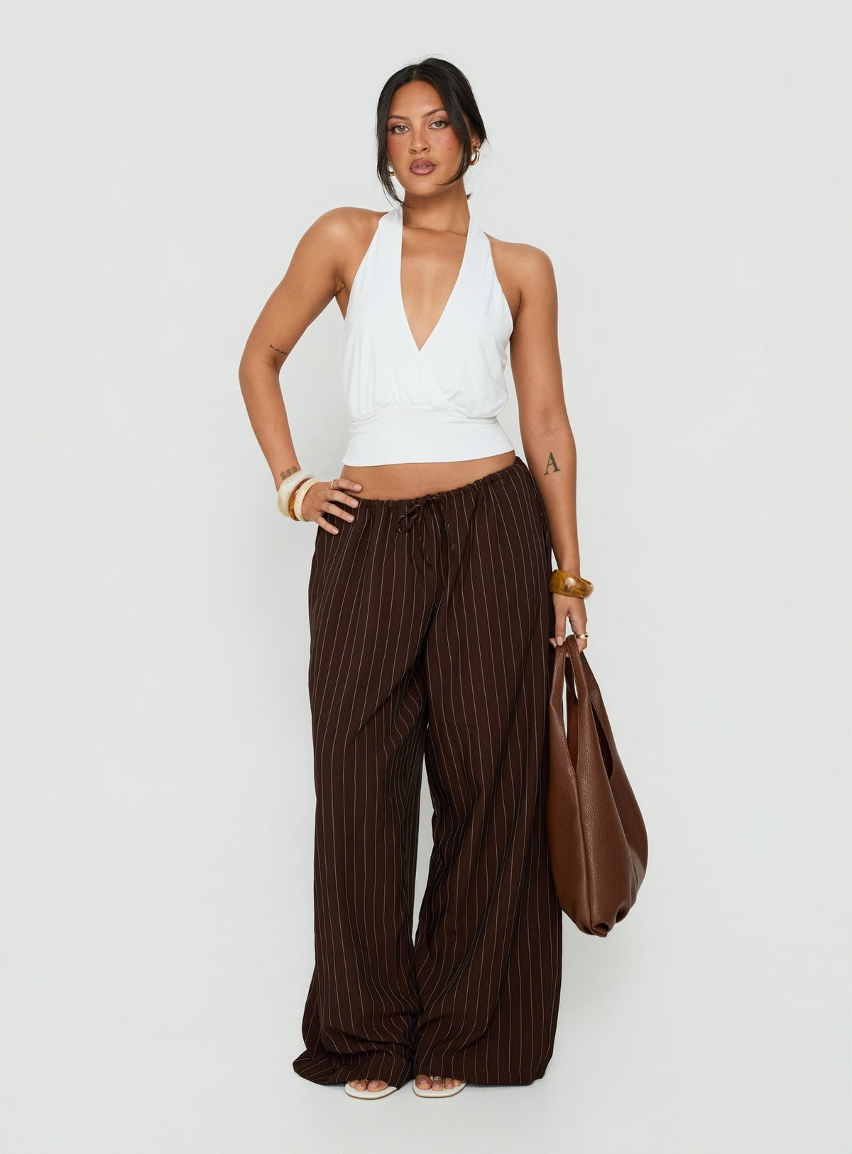 Featuring the Bungala Oversized Relaxed Pants Brown Pinstripe womens-regular-pants with mid-rise front view of model wearing Princess Polly