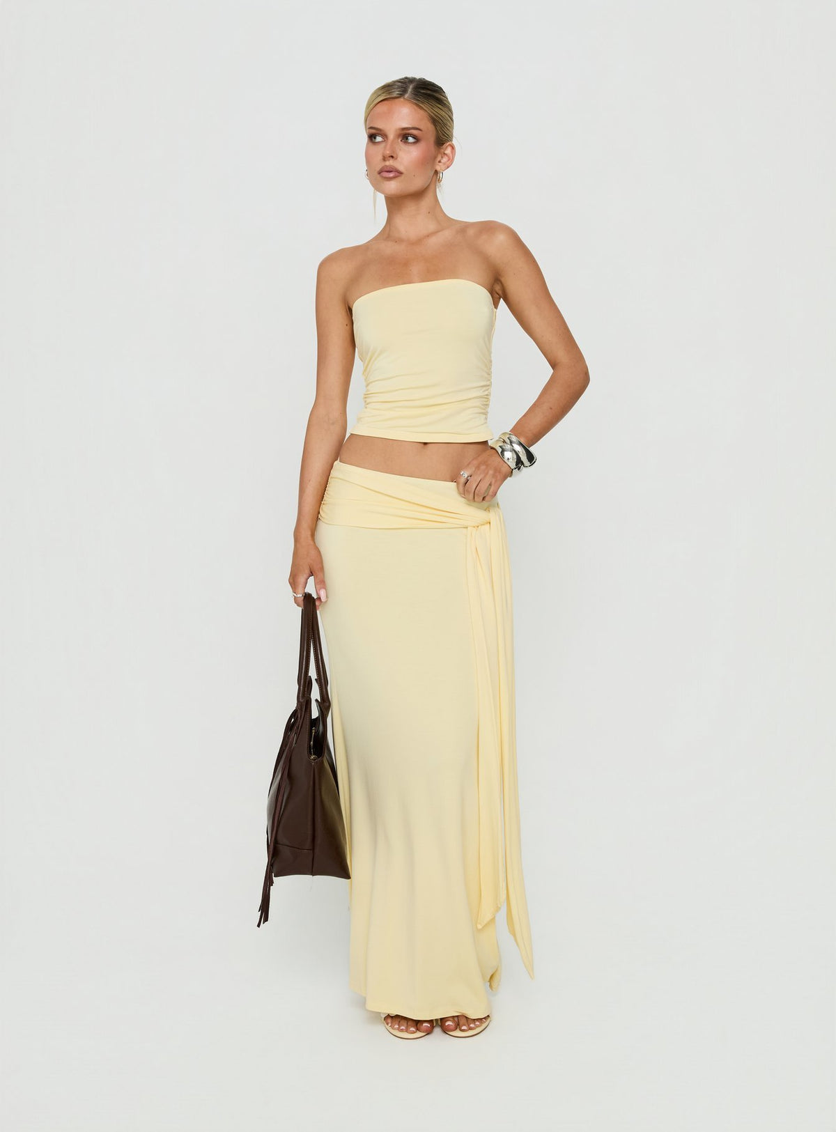 Featuring the Aymee Tie Detail Maxi Skirt in Yellow, a women's skirt with relaxed fit, lace hem, solid print, aline shape, and wrap details side view of model wearing Princess Polly