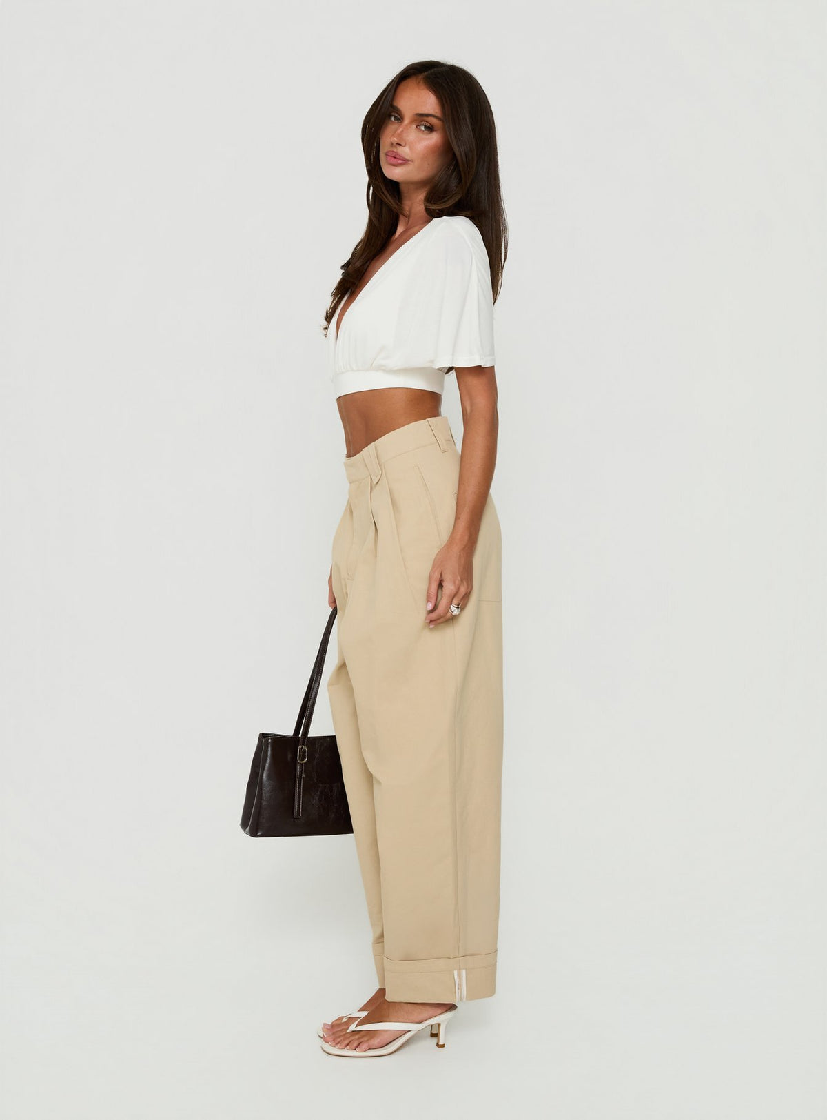 Crafted from tan fabric the Kendall Pant Sand womens-regular-pants with high-rise pleated wide-leg silhouette side view of model wearing