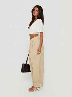Crafted from tan fabric the Kendall Pant Sand womens-regular-pants with high-rise pleated wide-leg silhouette side view of model wearing
