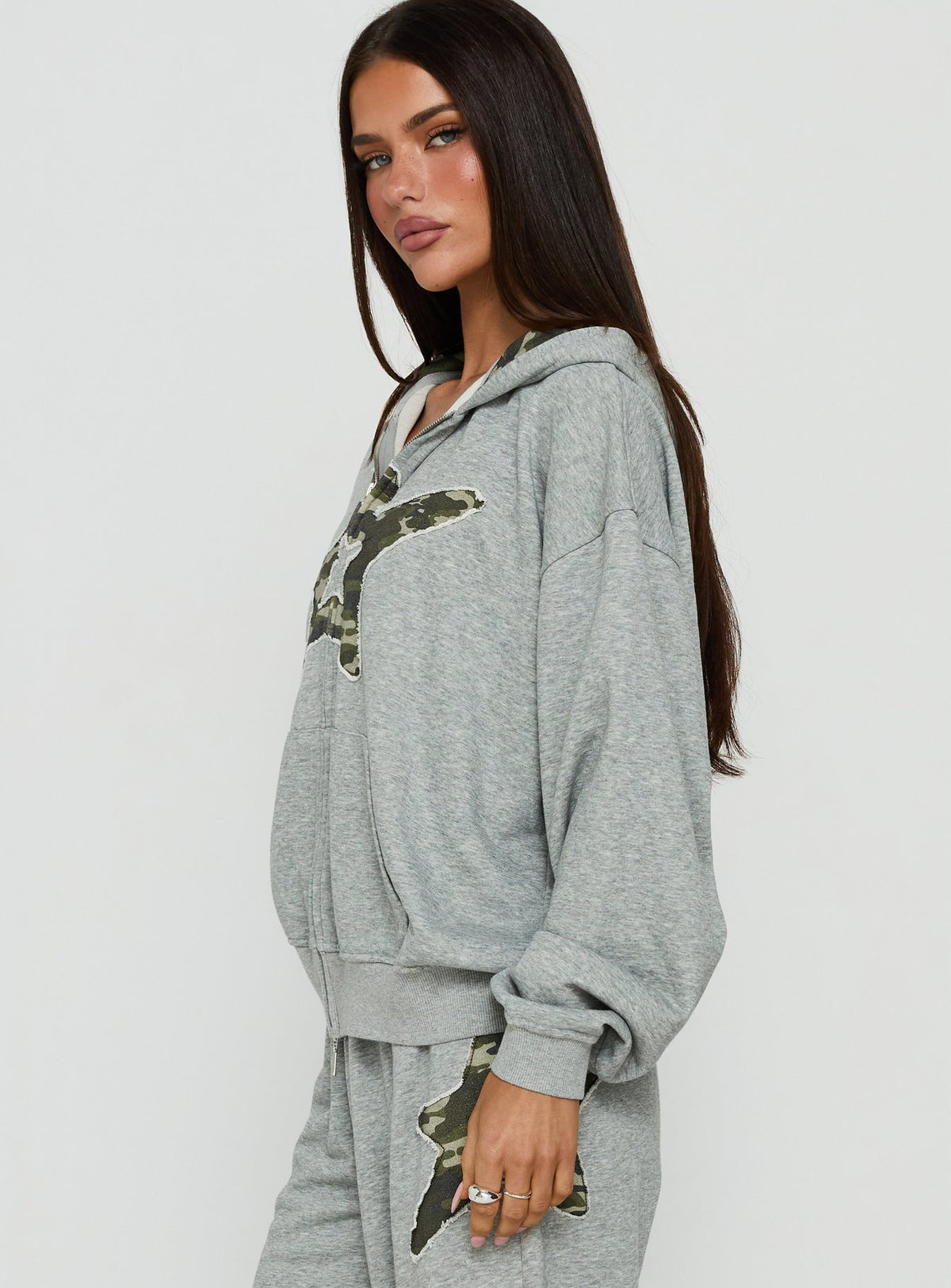 Designed with the Chelzie Zip Through Graphic Hoodie Grey Marle / Camo in womens jumpers featuring oversized fit, hood details, camo print, and short length side view of model wearing Princess Polly