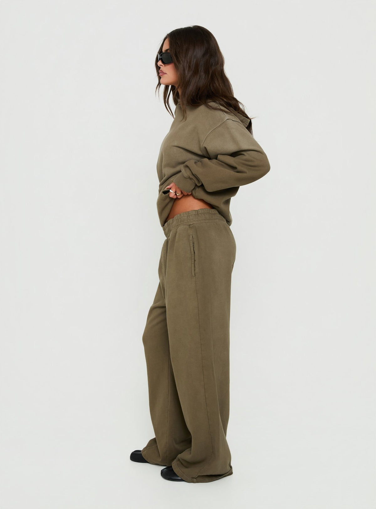 Highlighting the AT Fleece Baggy Sweatpant Washed Olive in womens-regular-pants with mid-rise wide-leg design side view of model wearing Princess Polly