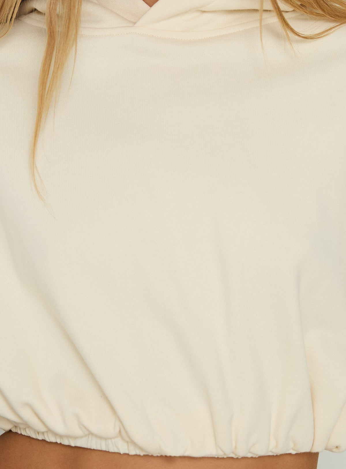 Highlighting the bubble hem detail of the Mayse Cropped Hoodie Cream womens jumpers in short length product Princess Polly